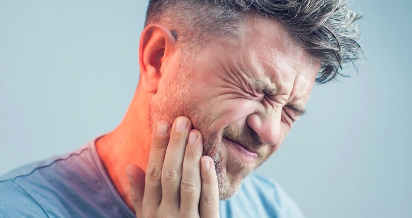 close up of a man with his face expressing pain. He is holding his jaw.