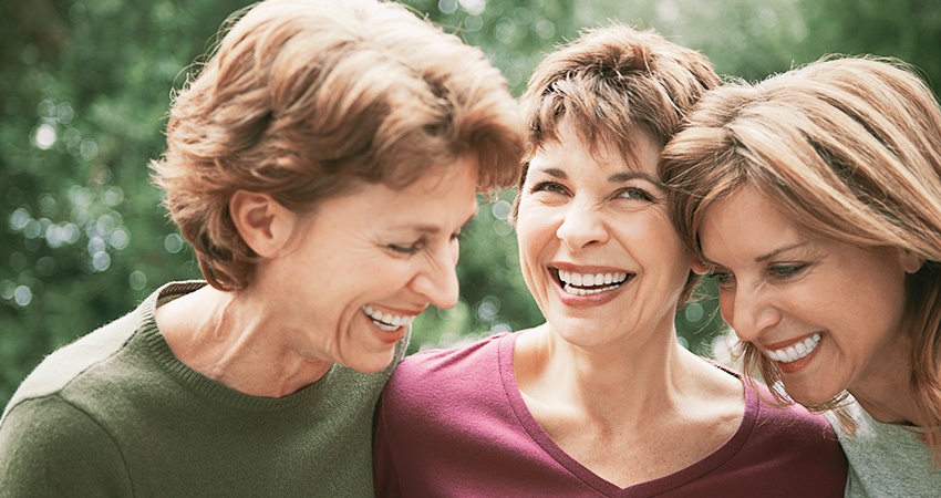Three senior women laugh and show their All-On-Four dental implants