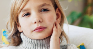 Close up of a young girl holding her jaw. She looks like she is in pain.